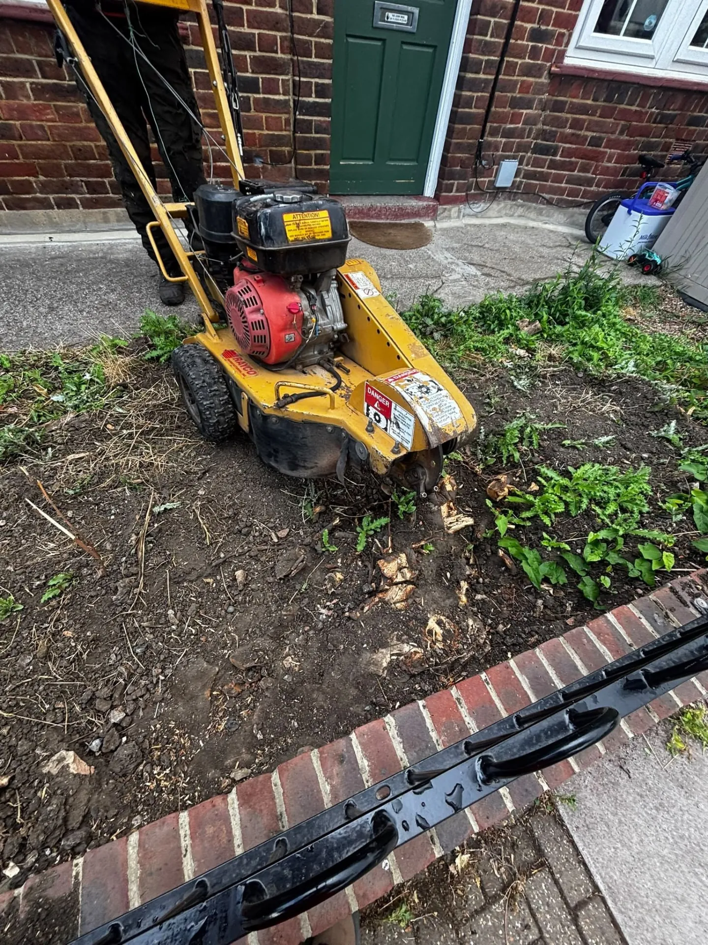 Stump grinder beside a ground-out stump in a front garden